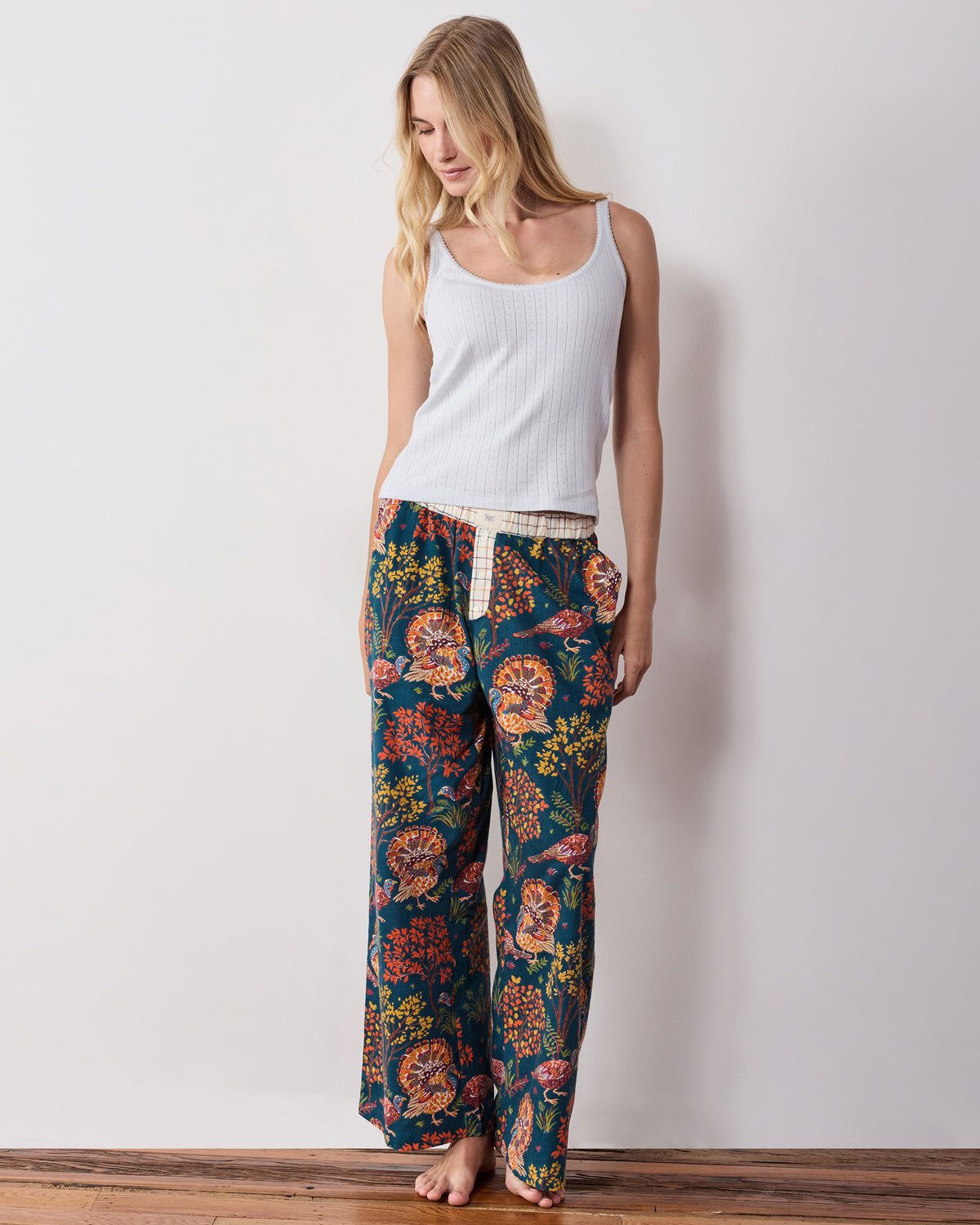 Full-length front view of the navy Turkey Trot pajama pants with a contrasting waistband and turkey print, styled with a white tank top.