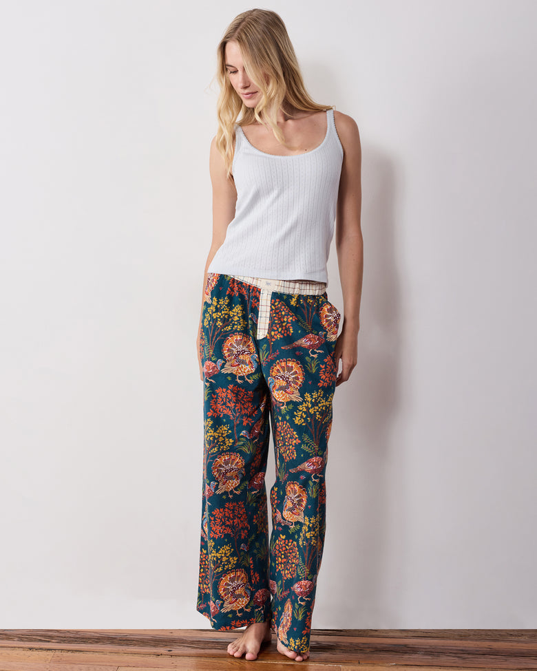 Full-length front view of the navy Turkey Trot pajama pants with a contrasting waistband and turkey print, styled with a white tank top.