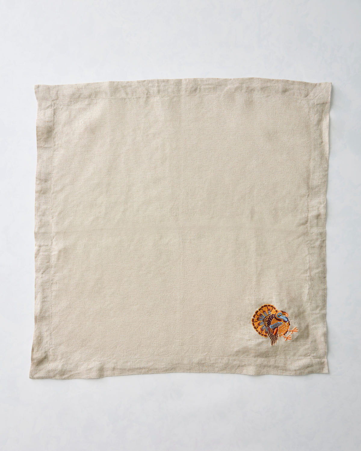 Natural dinner napkin with a small embroidered turkey near one corner.