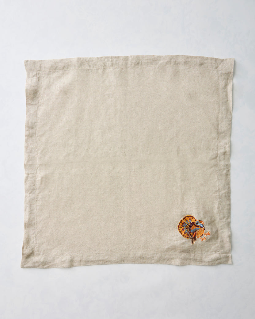 Natural dinner napkin with a small embroidered turkey near one corner.