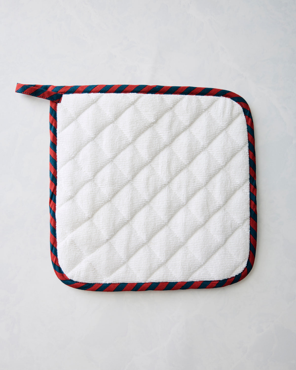 White quilted pot holder with navy-and-red striped binding and hanging loop.