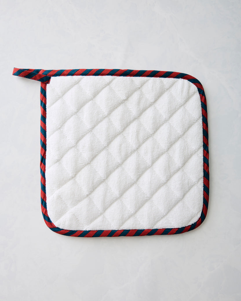 White quilted pot holder with navy-and-red striped binding and hanging loop.
