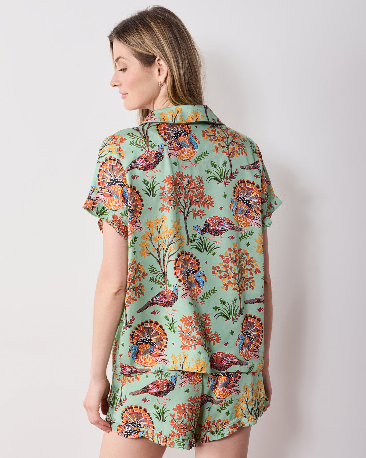 Back view of the soft sage Turkey Trot ruffle pajama set with a turkey-and-autumn-tree print, short-sleeved top, and ruffled shorts hem.