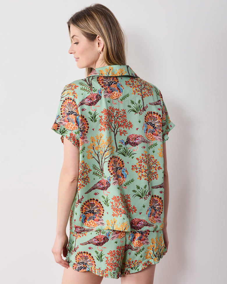 Back view of the soft sage Turkey Trot ruffle pajama set with a turkey-and-autumn-tree print, short-sleeved top, and ruffled shorts hem.