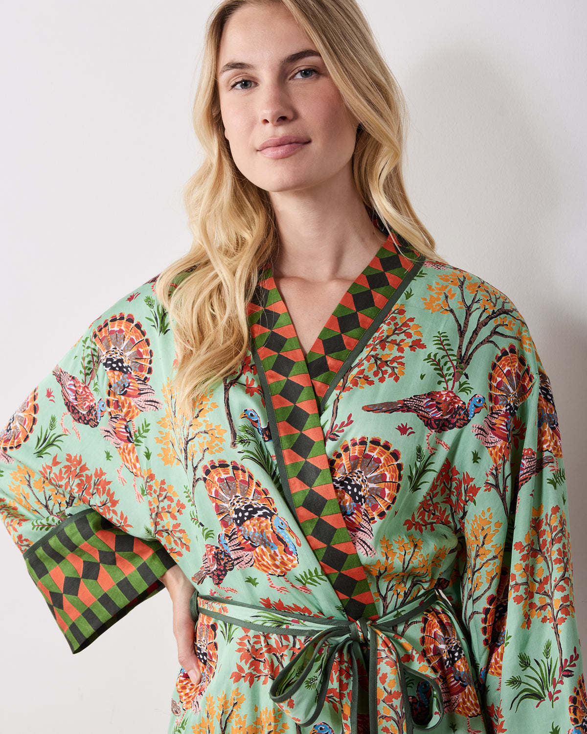 Front close-up of a soft sage Turkey Trot robe with a turkey-and-autumn-tree print, contrasting diamond-patterned collar and cuff, and tied waist.