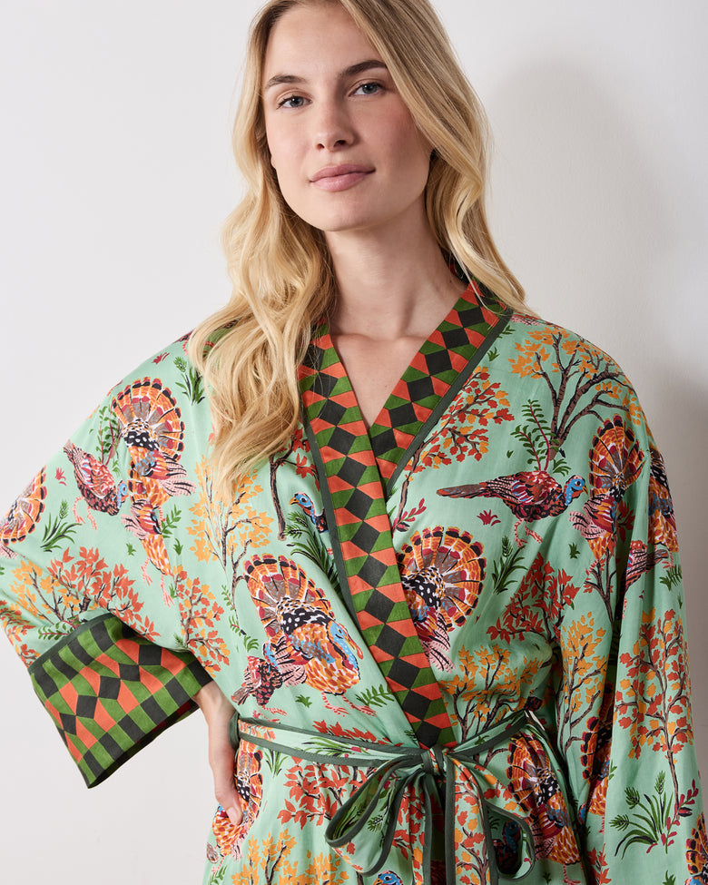 Front close-up of a soft sage Turkey Trot robe with a turkey-and-autumn-tree print, contrasting diamond-patterned collar and cuff, and tied waist.