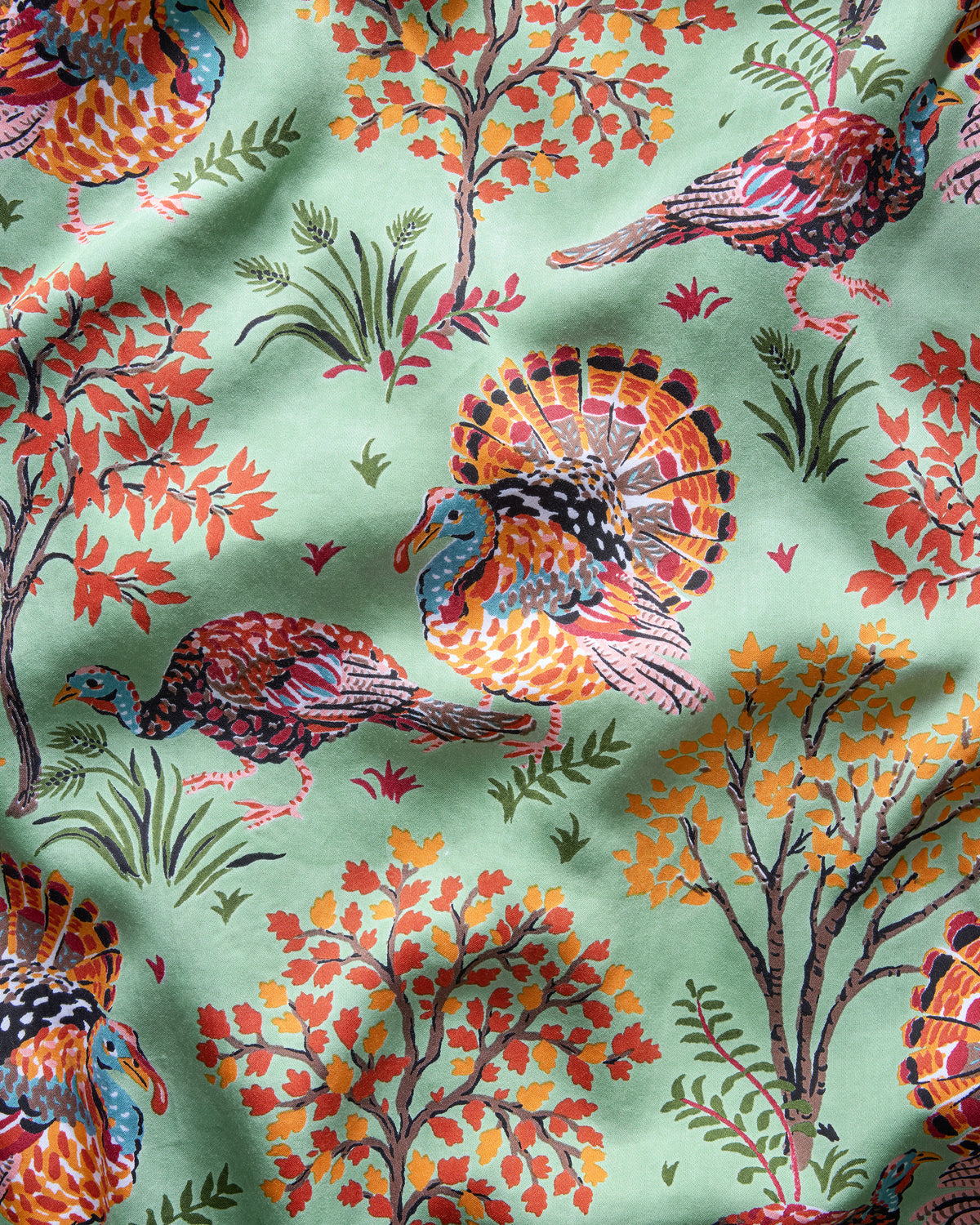 Close-up of a soft sage print featuring colorful turkeys, autumn trees, grasses, and leaves.