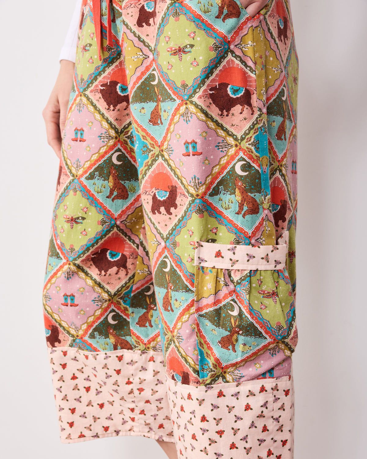 Close-up of Western Scenes patterned pants showing side pockets, cropped hems, and contrasting floral cuffs.