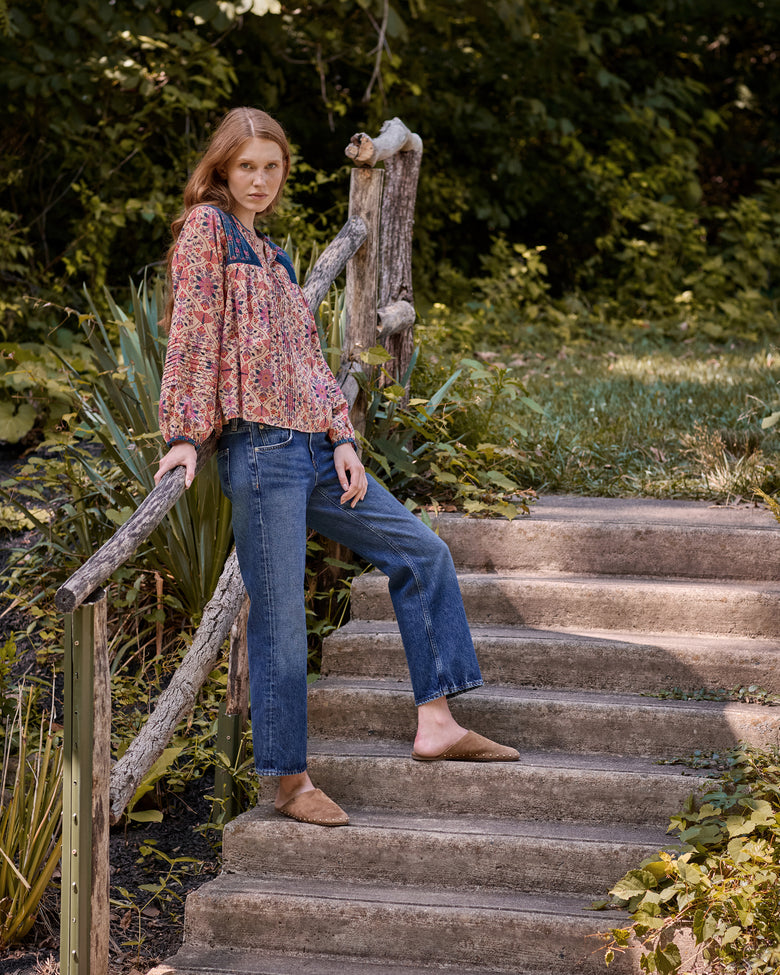 Model wearing the Winged Tapestry Denver Blouse with jeans on outdoor steps surrounded by plants.