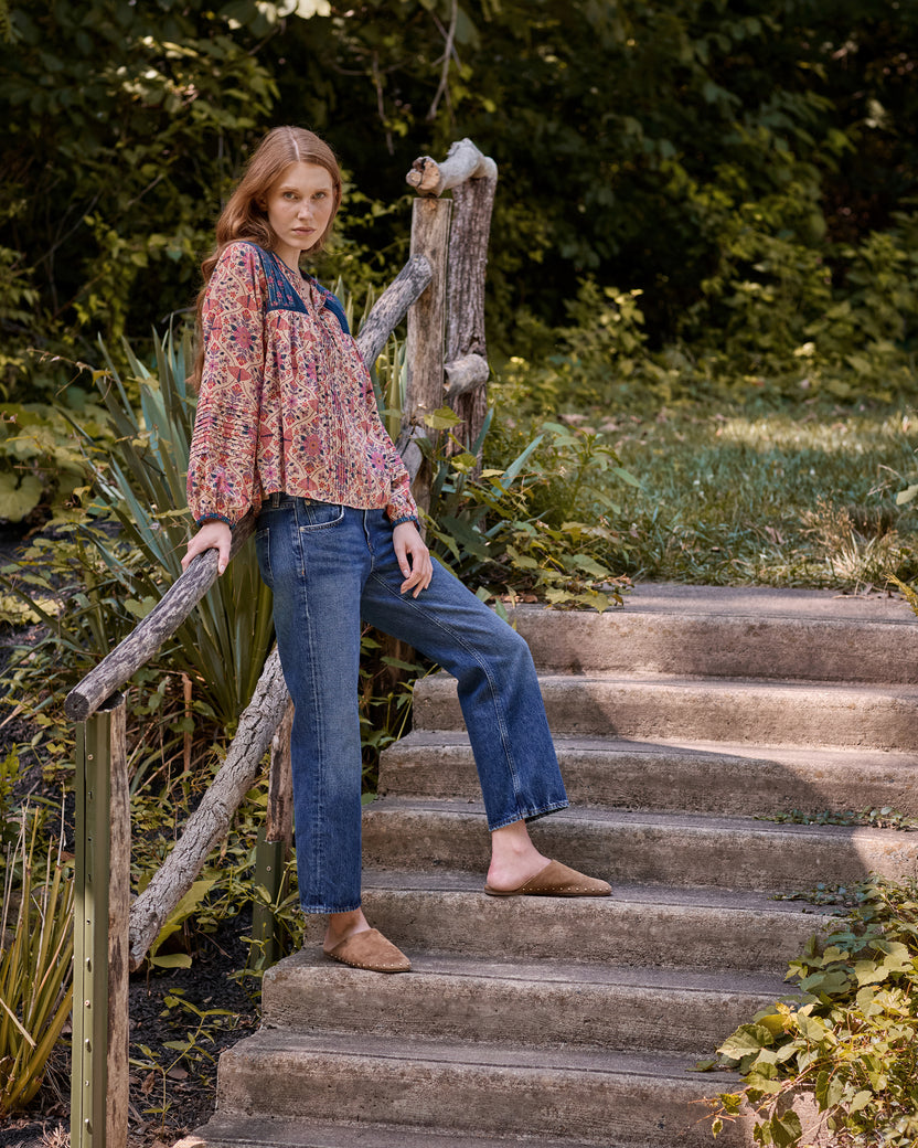 Model wearing the Winged Tapestry Denver Blouse with jeans on outdoor steps surrounded by plants.
