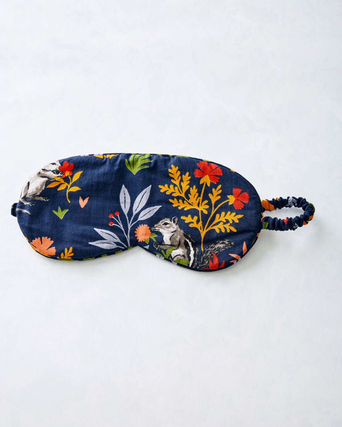 Indigo eye mask with woodland flowers, leaves, animal illustrations, and an elastic strap.