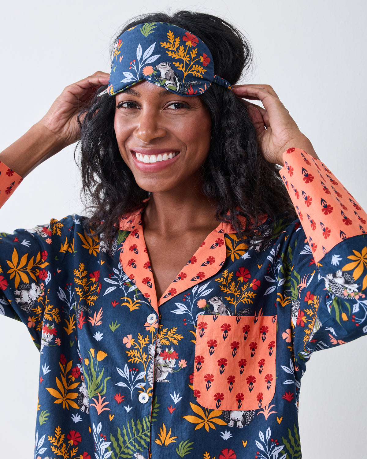 Person wearing the indigo Woodland Critters eye mask, showing its woodland print and adjustable side strap.