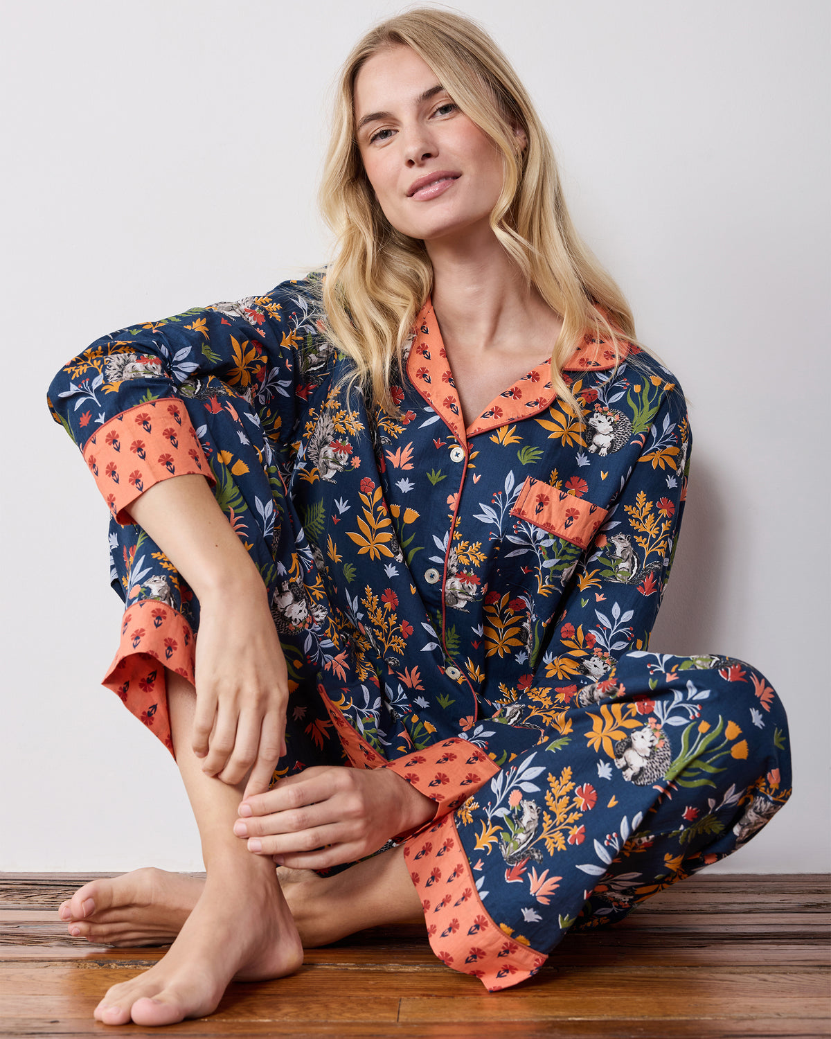 Person seated on a wooden floor wearing the indigo Woodland Critters long pajama set with a button-down top, long sleeves, and patterned pants.