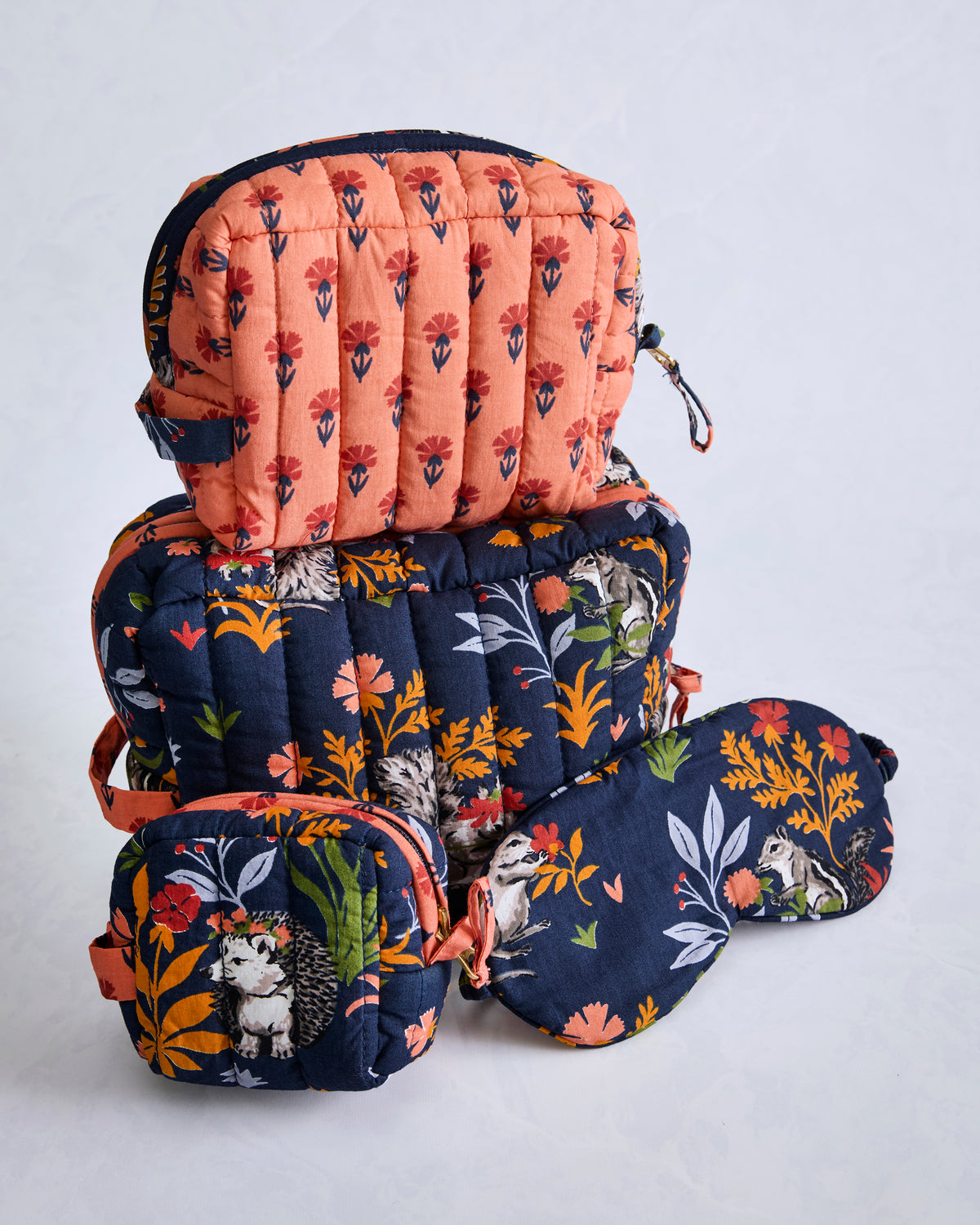 Three navy quilted pouches and a matching eye mask arranged in a stack, printed with woodland plants and animals.