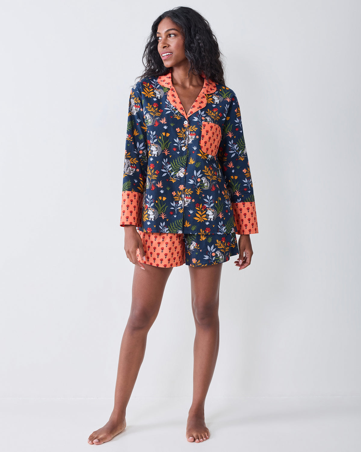 Full-length front view of a person wearing the indigo Woodland Critters pajama set with contrasting coral cuffs and shorts panel.