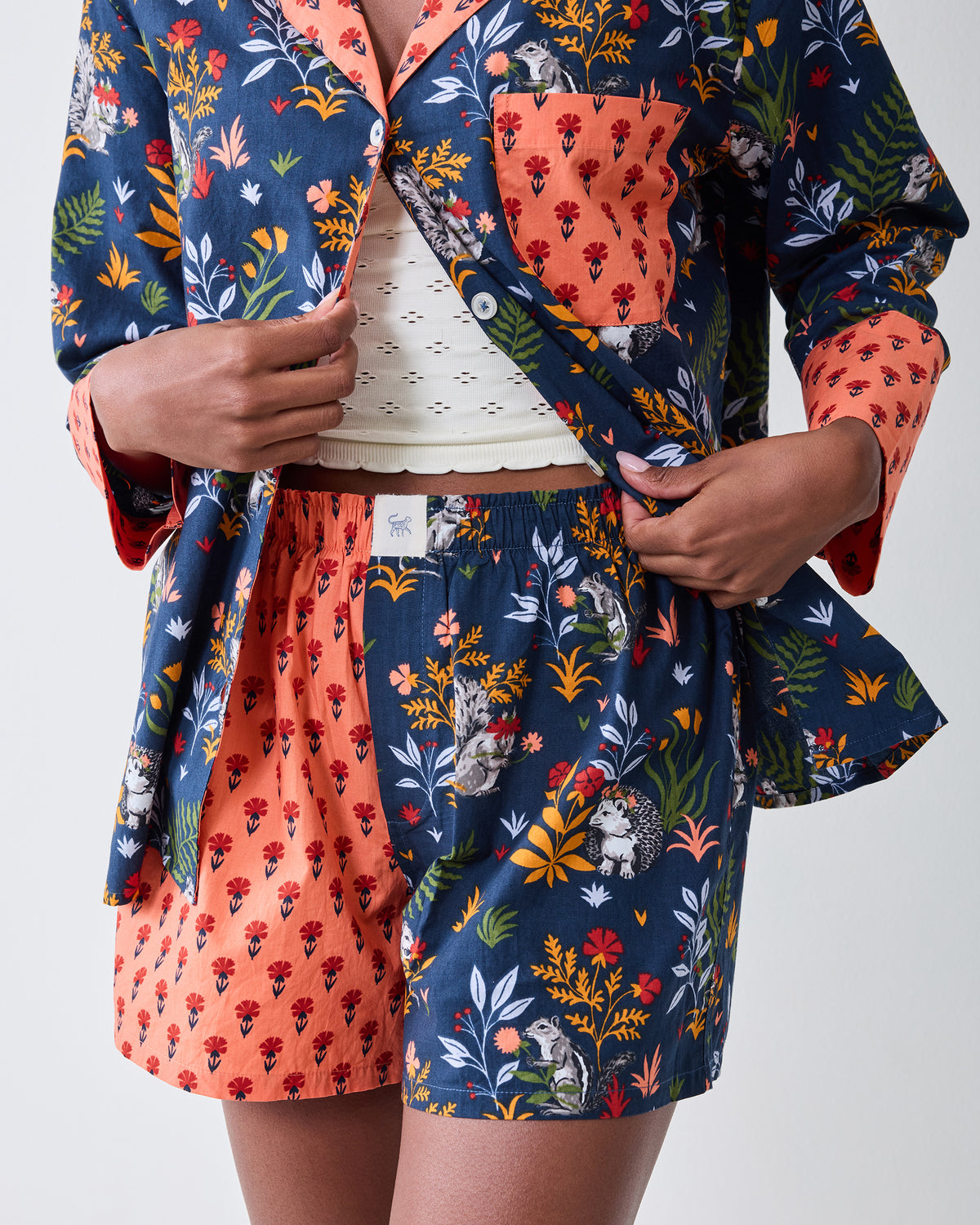 Close-up of the indigo Woodland Critters pajama top and coordinating shorts, showing the coral trim, pocket, buttons, and elastic waistband.