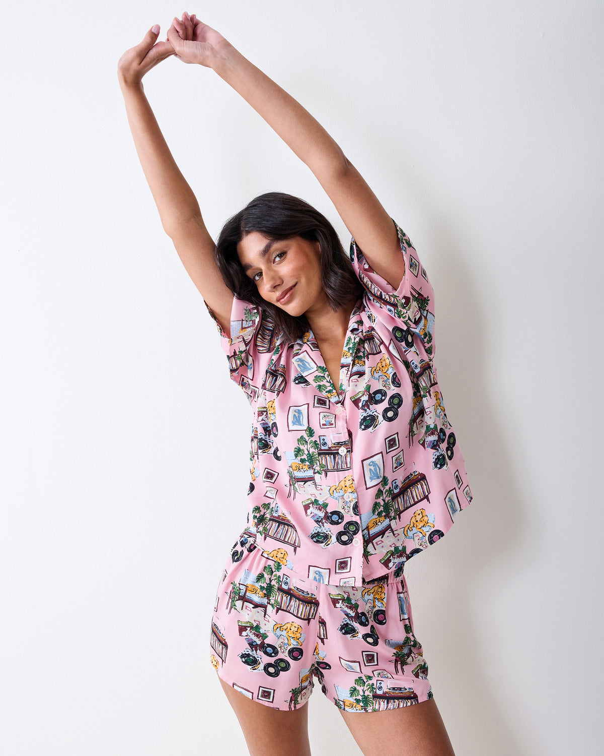 Model wearing the pink printed Eco Satin Sweet Dreams pajama set with a button-front top and shorts, arms raised.