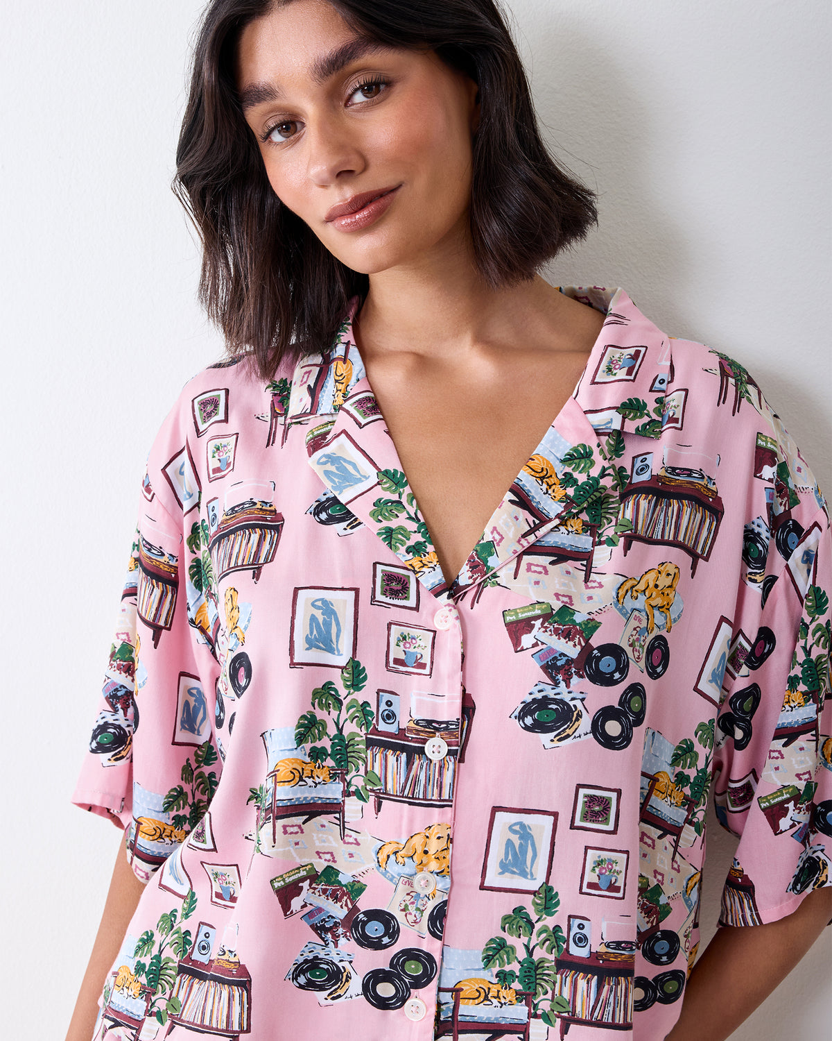 Close-up of the pink printed pajama top showing its notched collar, front buttons, short sleeves, and record-themed pattern.