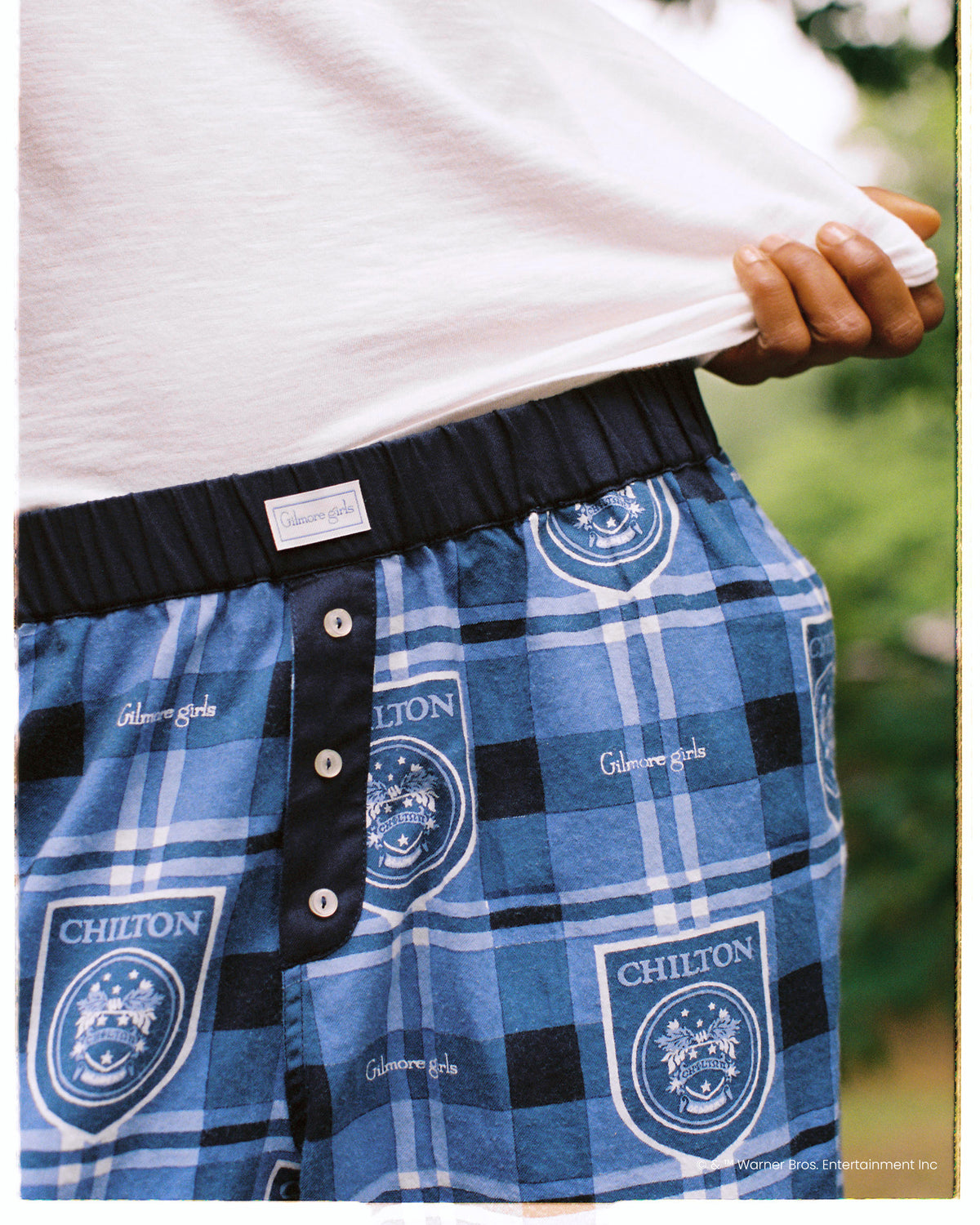 Close-up of the blue plaid Chilton pajama pants showing the elastic waistband, button fly, and printed crests.