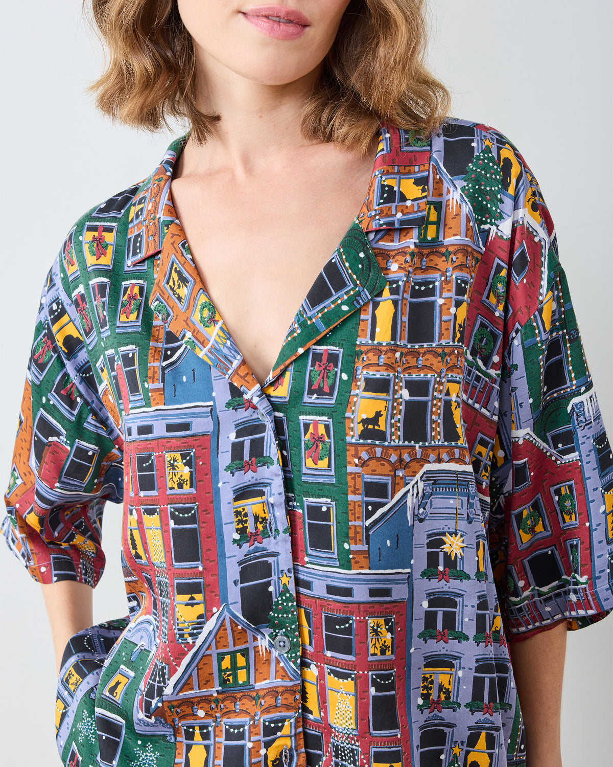 Close-up of the Manhattan Christmas pajama top showing its notched collar, buttons, short sleeves, and colorful brownstone holiday print.