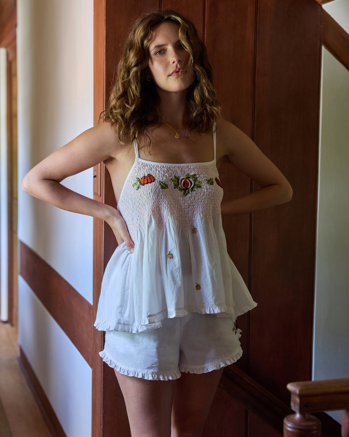 Person wearing a natural-colored embroidered pumpkin camisole and ruffled shorts set indoors.