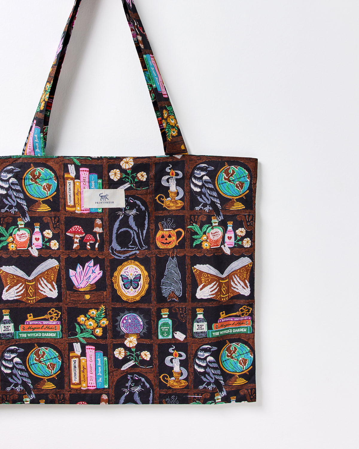 Close-up of the Enchanted Study tote bag showing its illustrated raven, globe, cat, books, candle, and botanical print.
