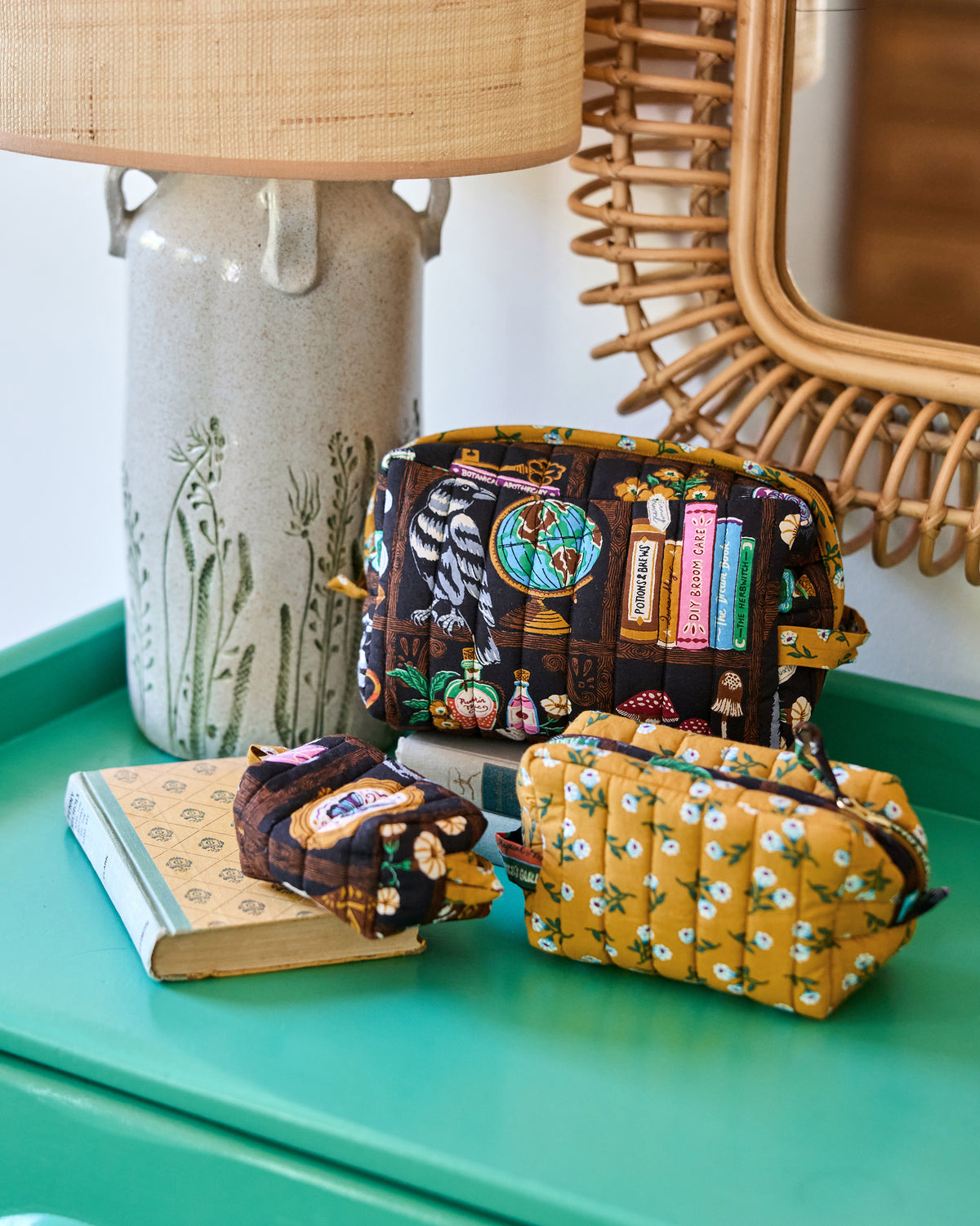 Three Enchanted Study quilted pouches in different sizes, displayed together on books and a green tabletop.