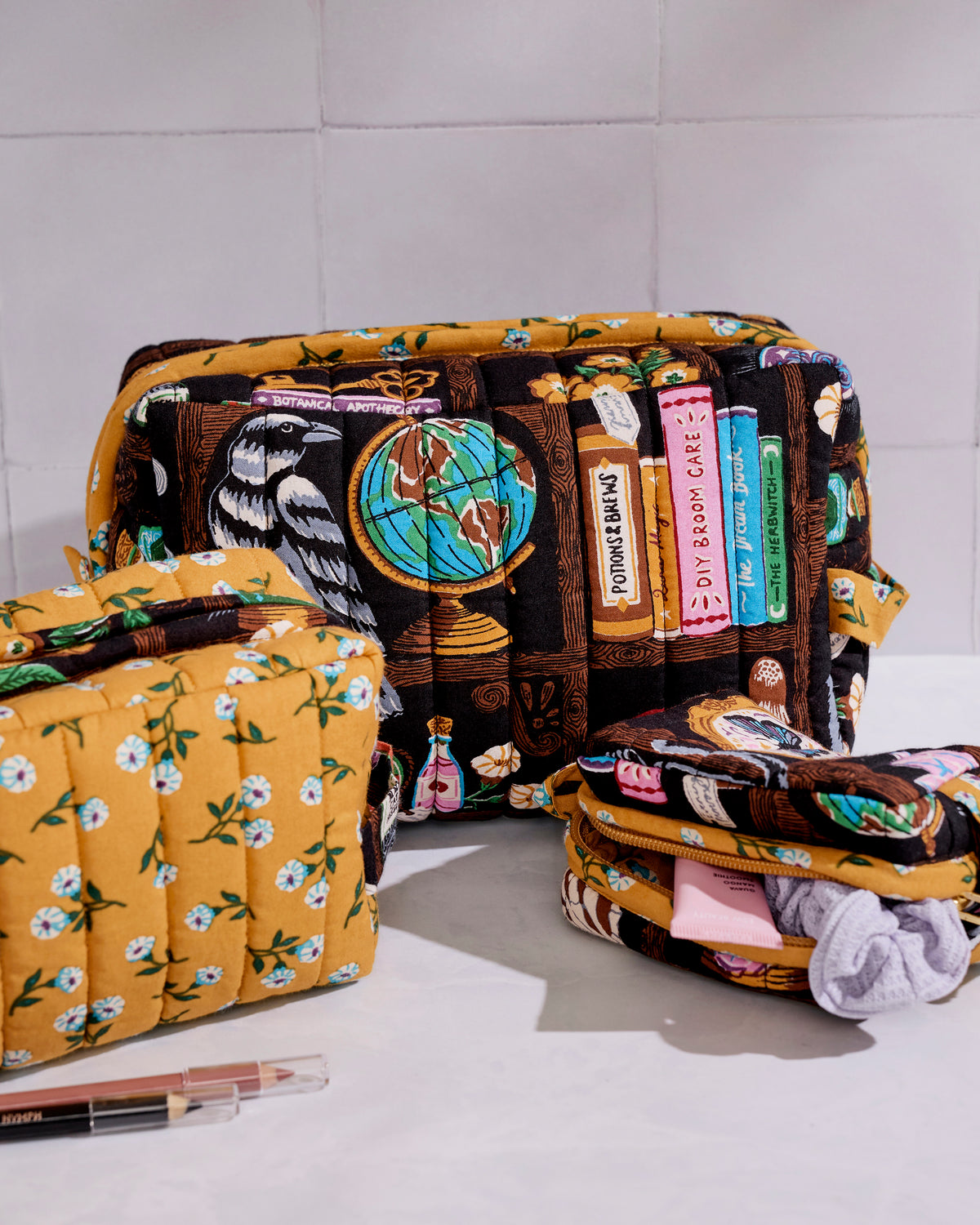 Three quilted zip pouches in different sizes displayed together, including a floral pouch, a study-themed pouch, and an open pouch with fabric inside.