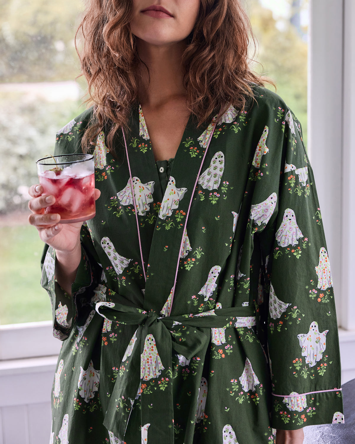 Close view of a dark green ghost-and-floral print getting-ready robe with a matching belt, worn while holding a drink.