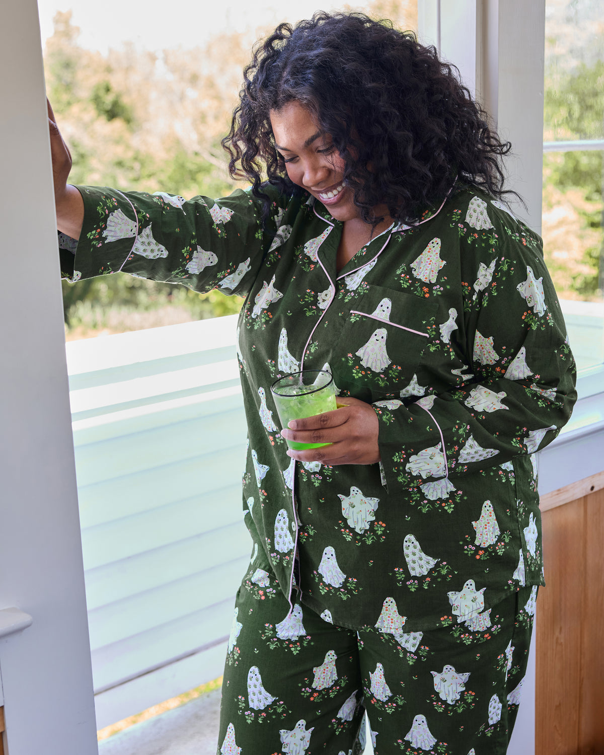 Close view of a dark green ghost-print long-sleeve pajama top and matching pants with contrasting piping and chest pocket.