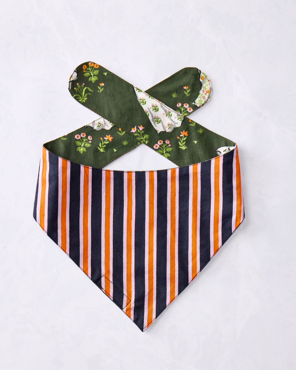 Pet bandana displayed flat with vertical orange, navy, and light stripes and green floral ghost-print ties.