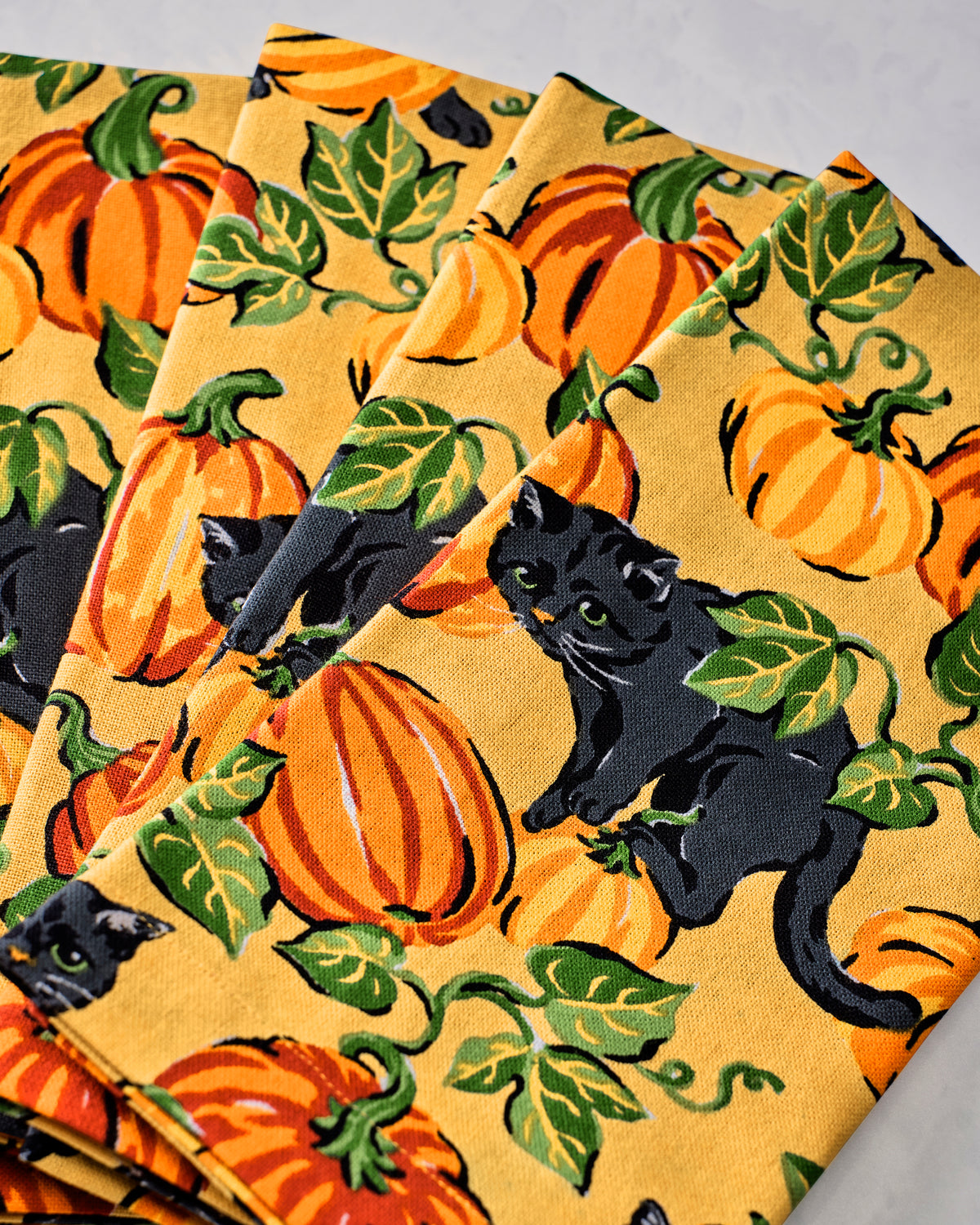Close-up of dinner napkin fabric printed with orange pumpkins, green leaves, and black cats.