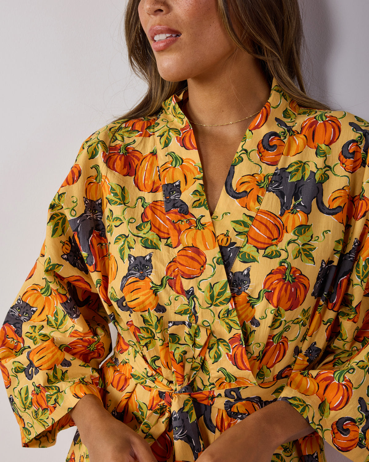 Close-up of the Pumpkin Prowl robe’s notched neckline, tied belt, sleeve, and pumpkin and black-cat print.