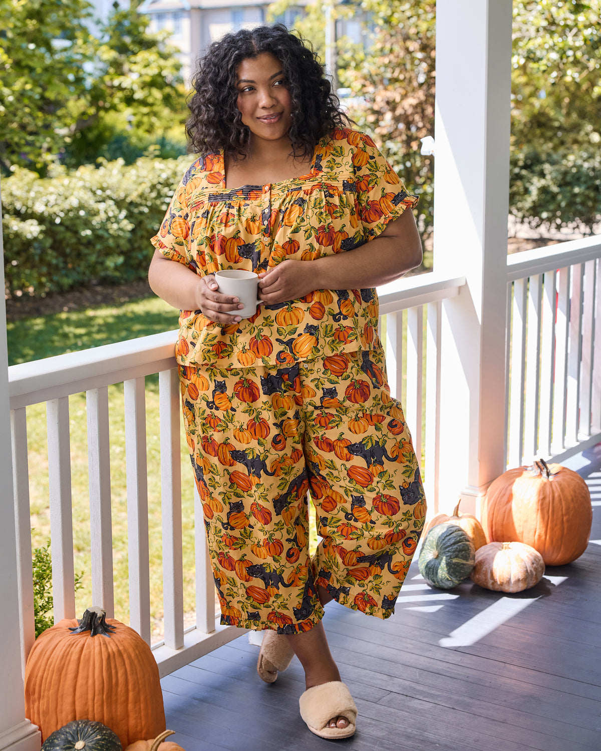 Person standing on a porch wearing the Pumpkin Prowl cropped pajama set with a pumpkin and black-cat print.