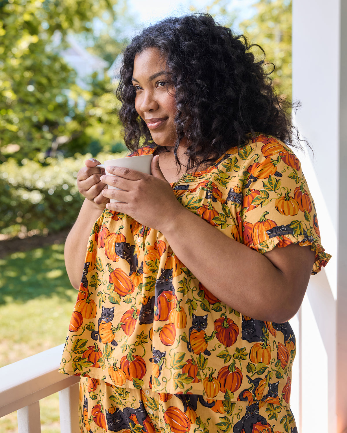 Person holding a mug while wearing the Pumpkin Prowl cropped pajama set with pumpkin and black cat print.