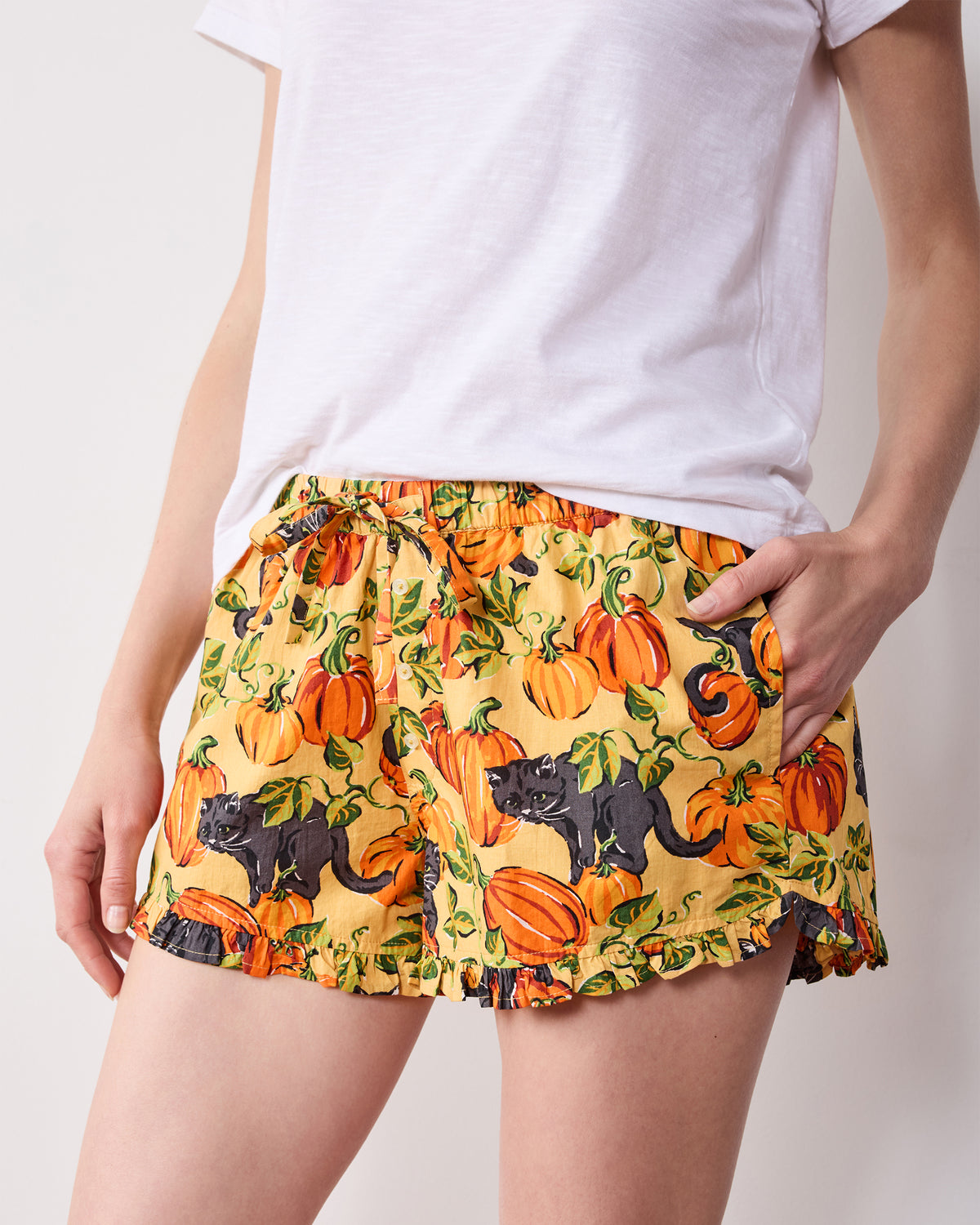 Front close-up of Pumpkin Prowl salted caramel ruffle pajama shorts with an elastic drawstring waistband, pockets, and pumpkin-and-black-cat print.