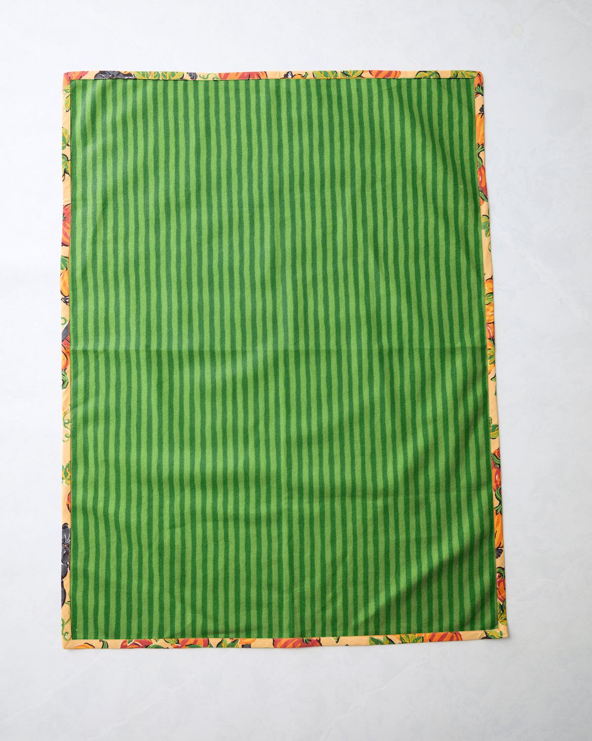 Tea towel showing a green vertically striped side with a narrow pumpkin-and-cat patterned border.