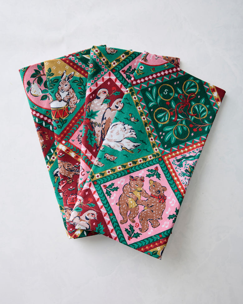 Folded set of four dinner napkins with a multicolored 12 Days of Christmas print featuring holiday illustrations.