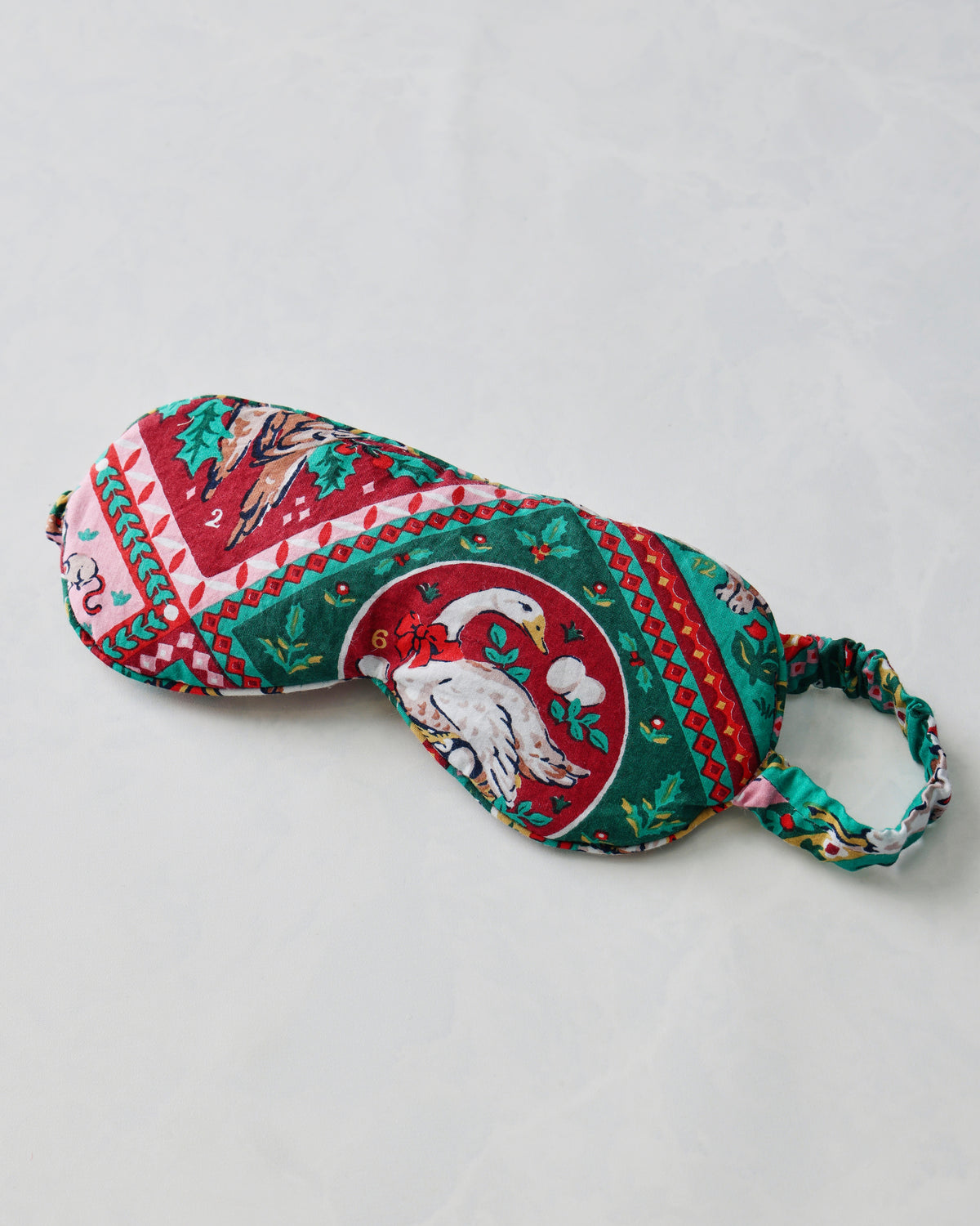 Eye mask with an elastic strap and a colorful vintage holiday print featuring a white bird in a circular motif.