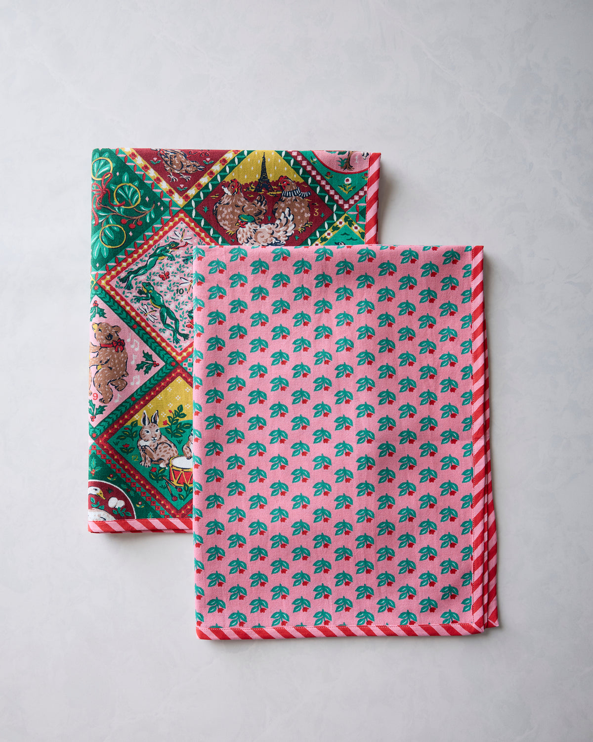 Two Christmas-themed tea towels shown together, one displaying the illustrated diamond pattern and the other showing a repeating leaf pattern with striped edging.