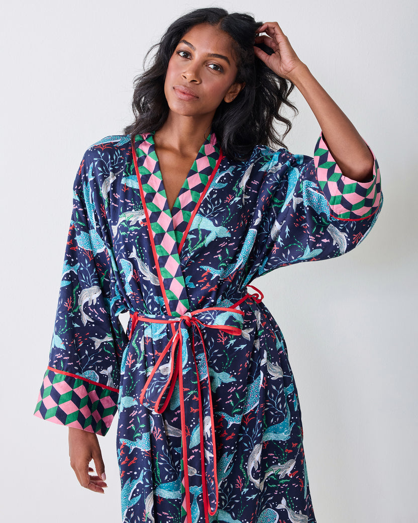 Front view of a model wearing the navy Arctic Sea Life Eco Satin Robe, showing the whale-and-underwater-flora print, contrasting geometric trim, belt, and wide cuffs.