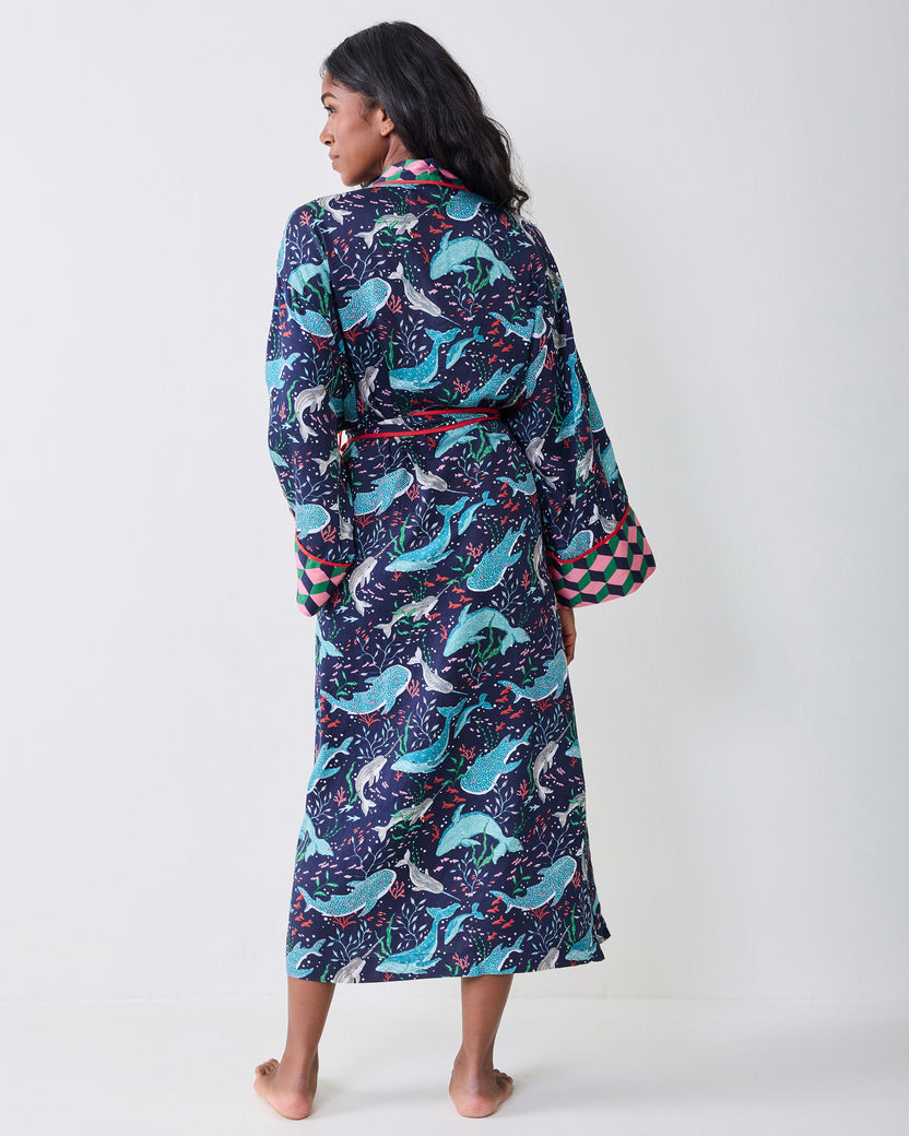 Back view of a model wearing the navy Arctic Sea Life Eco Satin Robe, showing the full whale-and-underwater-flora print, belt, and contrasting cuffs.