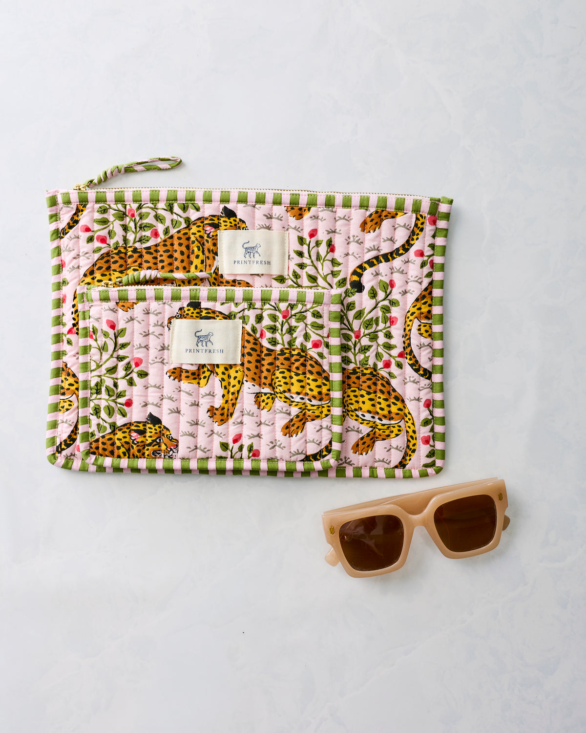 Two pink leopard-print zippered pouches displayed together beside sunglasses.