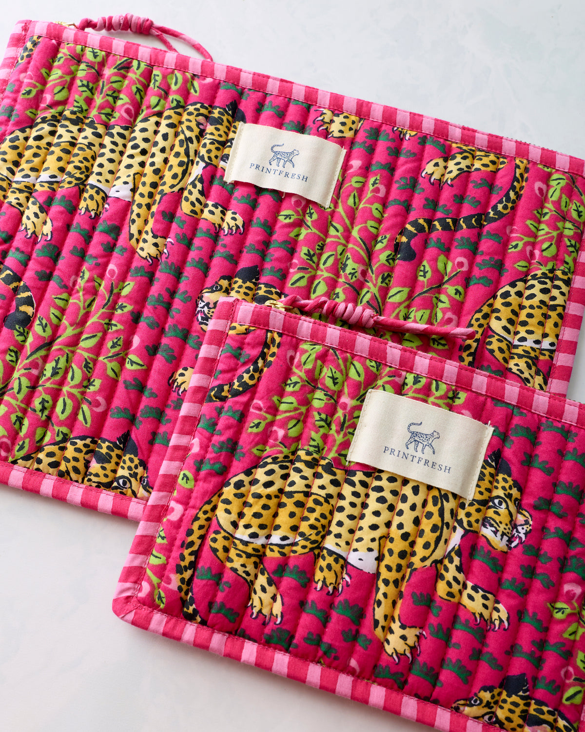 Close-up of two hot pink flat pouches showing the yellow leopard and green foliage print, gathered zipper pulls, and Printfresh labels.