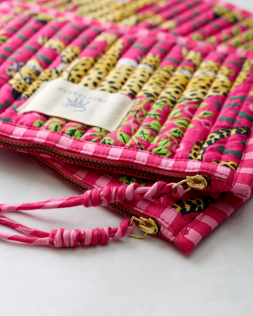 Close-up of the hot pink flat pouches showing their printed fabric, zippers, gold-tone zipper pulls, and tied fabric cords.