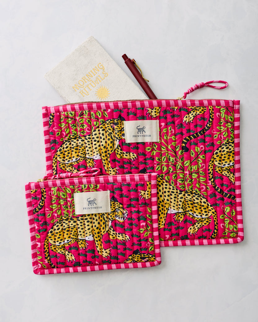Two hot pink flat pouches with yellow leopard and green foliage print, shown with a pen and a cream item labeled “MORNING ROUTINES.”