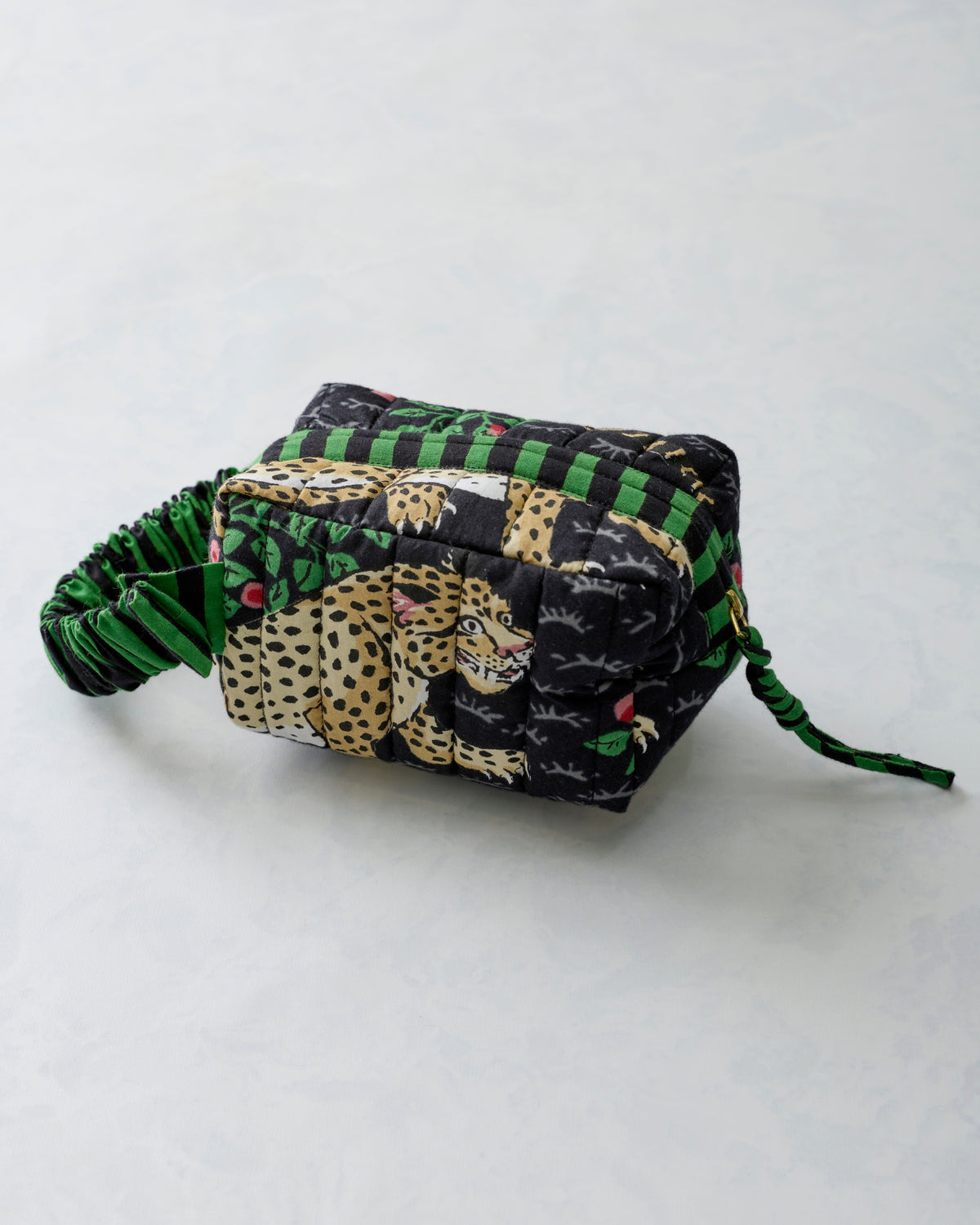 Side view of the Bagheera Ink quilted essentials wristlet with leopard print, green-and-black stripes, and a wrist strap.