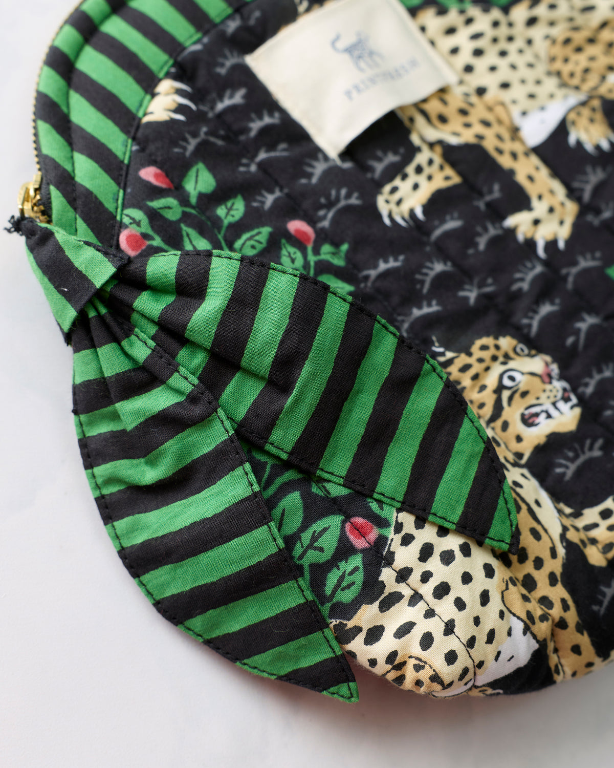 Close-up of the Bagheera Ink makeup bag showing striped trim, leopard-and-leaf print, zipper edge, and wrist loop.