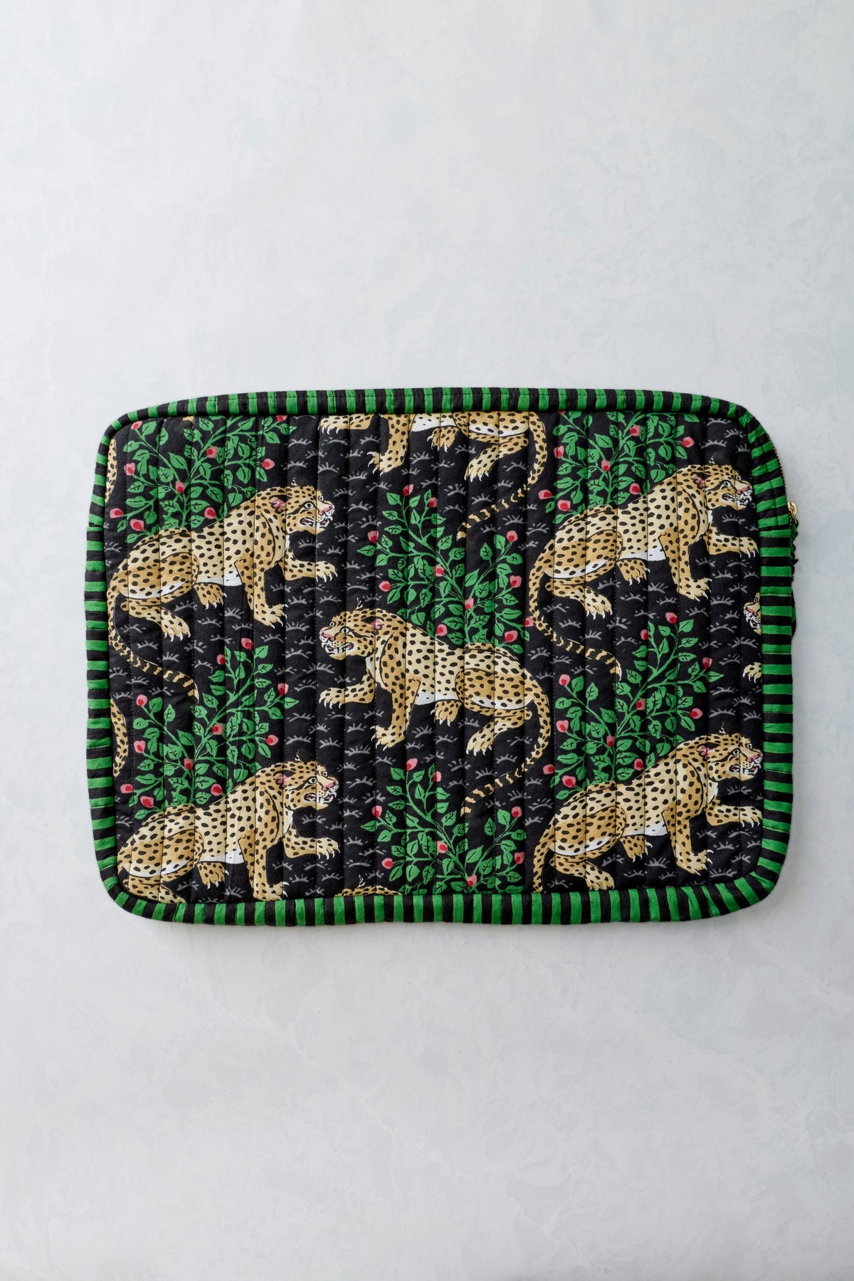 Front view of the Bagheera Ink quilted laptop sleeve with leopard and leafy print and a green-and-black striped border.