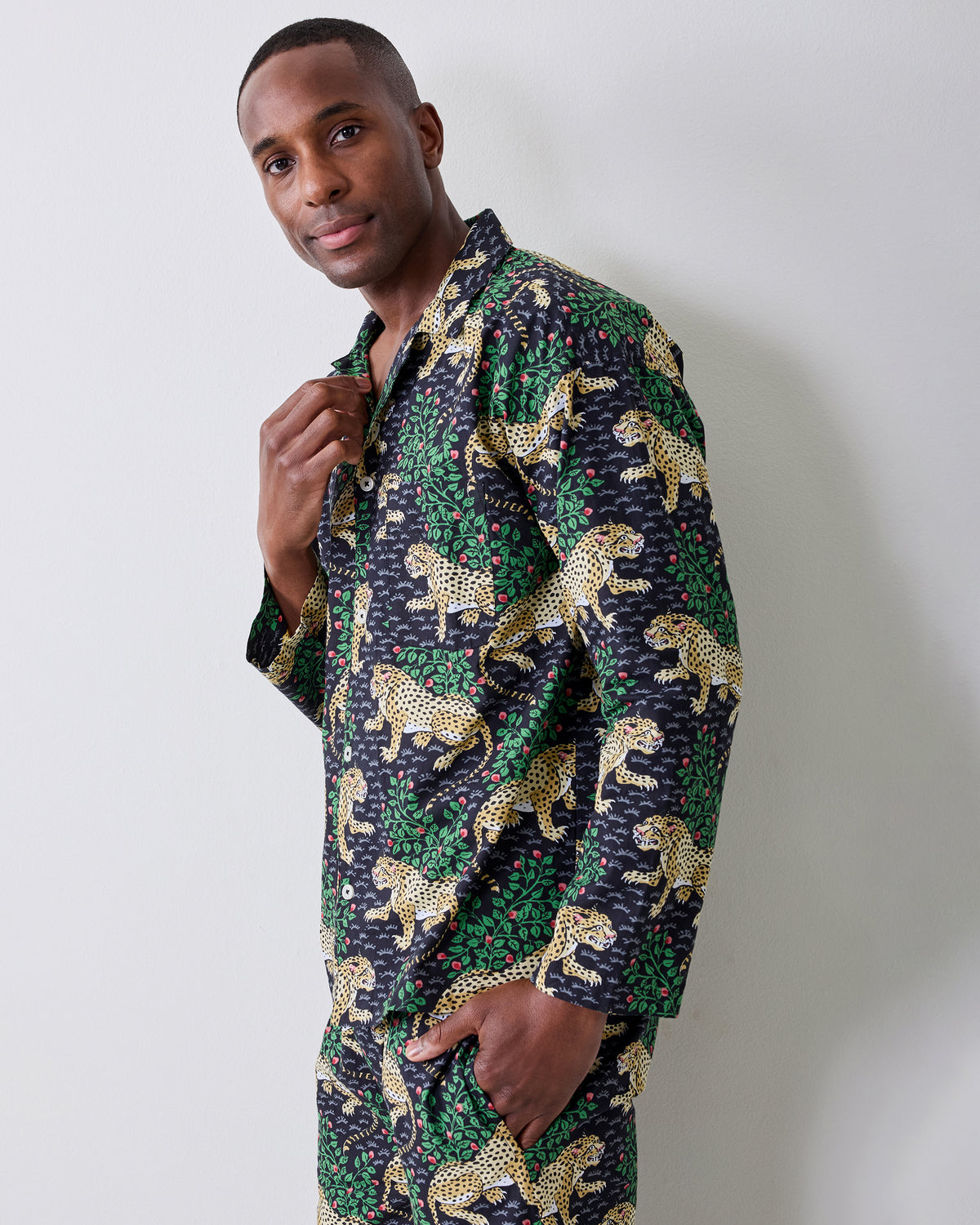 Person standing at a three-quarter angle wearing a dark patterned button-front shirt and matching trousers with yellow spotted cats and green foliage.
